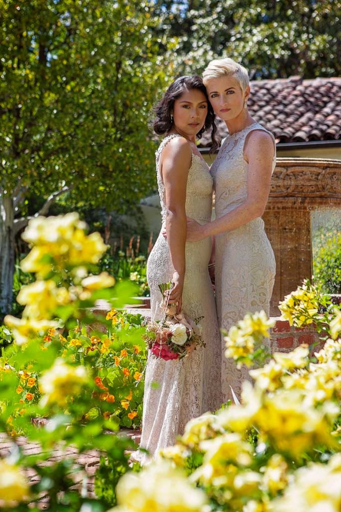 two lesbian brides at rustic Mexican wedding in a lace BHLDN wedding gown and lace jumpsuit with exposed back and holding bouquets