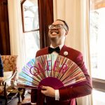 a groom waving a fan that says "queer"