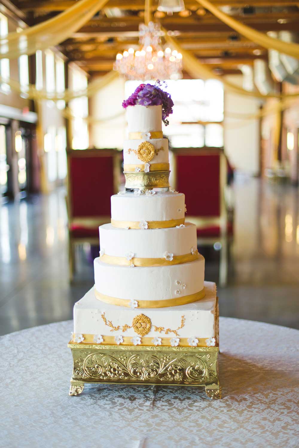 A six-tiered lemon cake with butter cream frosting embellished with gold accents and purple flowers. 