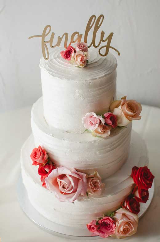 white wedding cake with red and pink flowers and a laser cut wedding cake topper with the word finally -- for an atlanta lesbian wedding