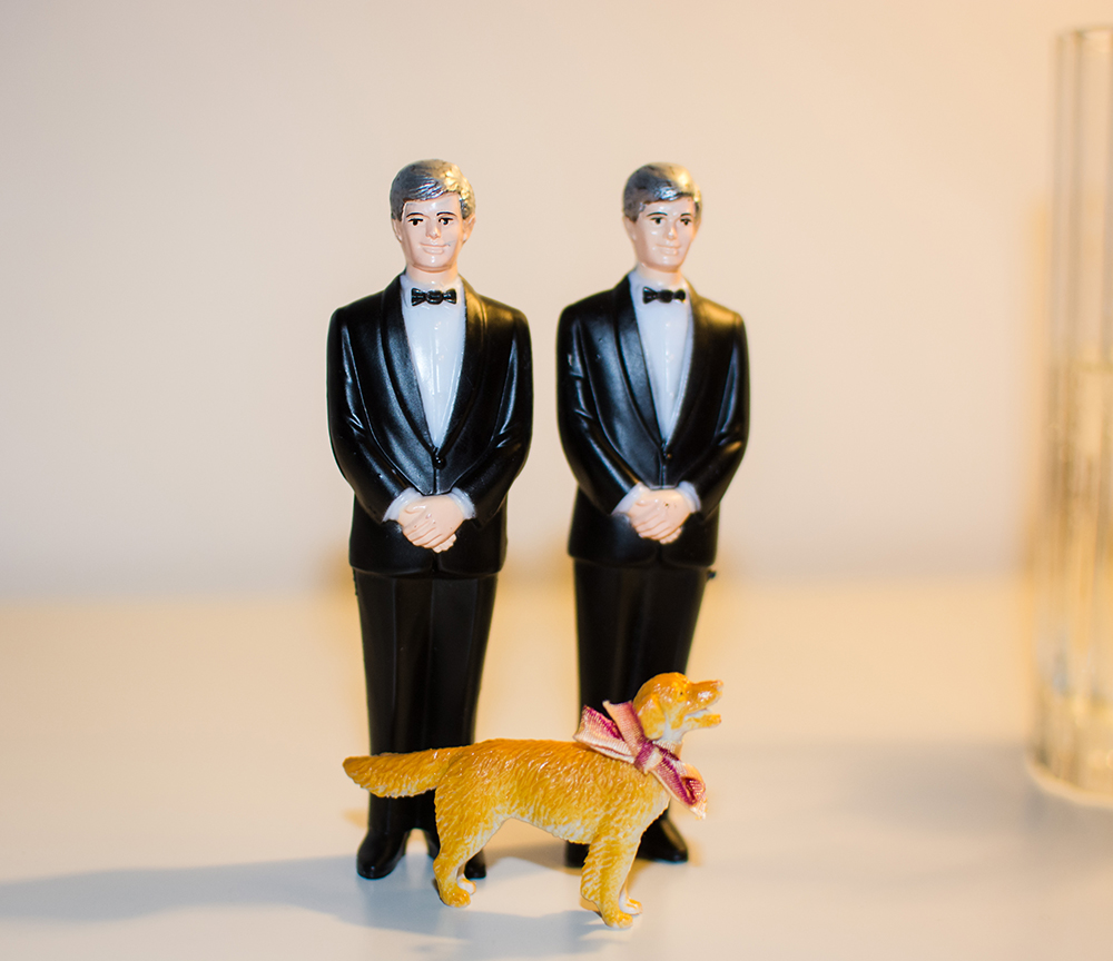 A cake topper with two grooms and their dog.