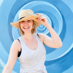 Mandy Roberts, yoga teacher and Soul Nourish Retreats leader Smiling blonde woman in a tanktop and a hat, blue swirling graphic in blackground