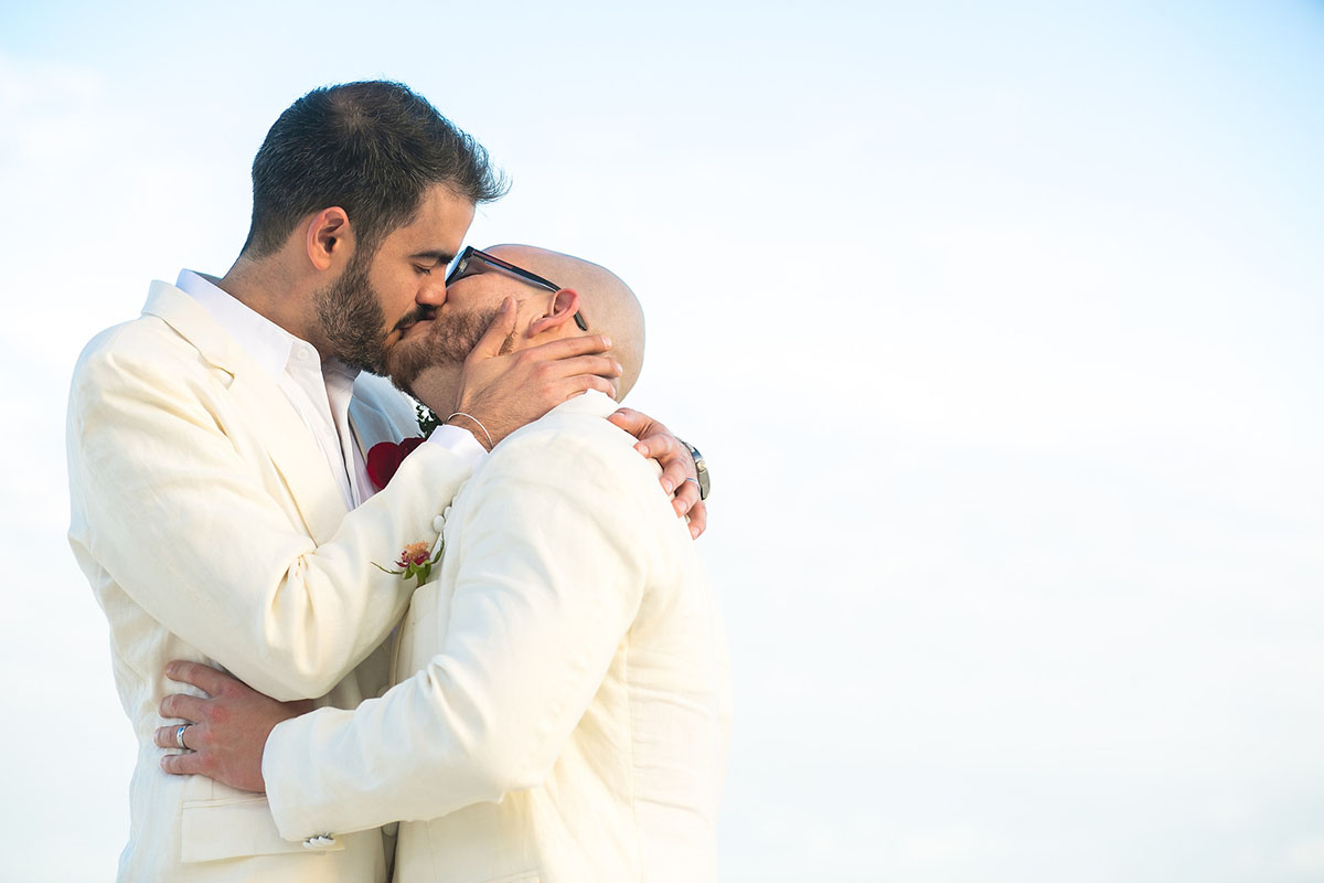 Destination Mexican beach wedding at Akiin Tulum two grooms white suits tuxedos kissing