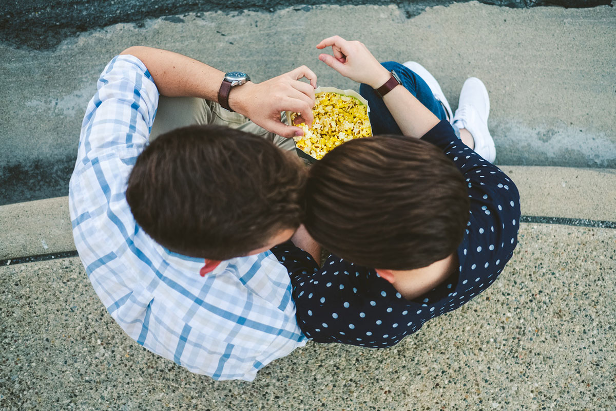 Fun, whimsical movie theater engagement sharing popcorn two grooms