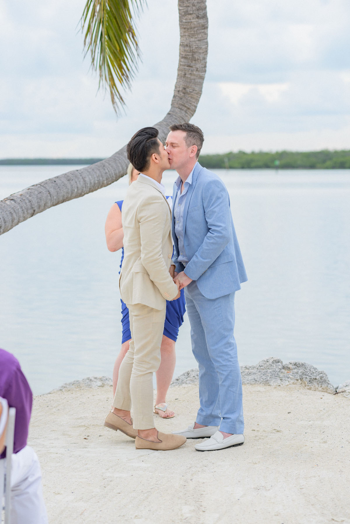 Intimate Florida Keys tropical wedding two grooms blue tan tuxedo sitting cheers kisses beach sand palm tree