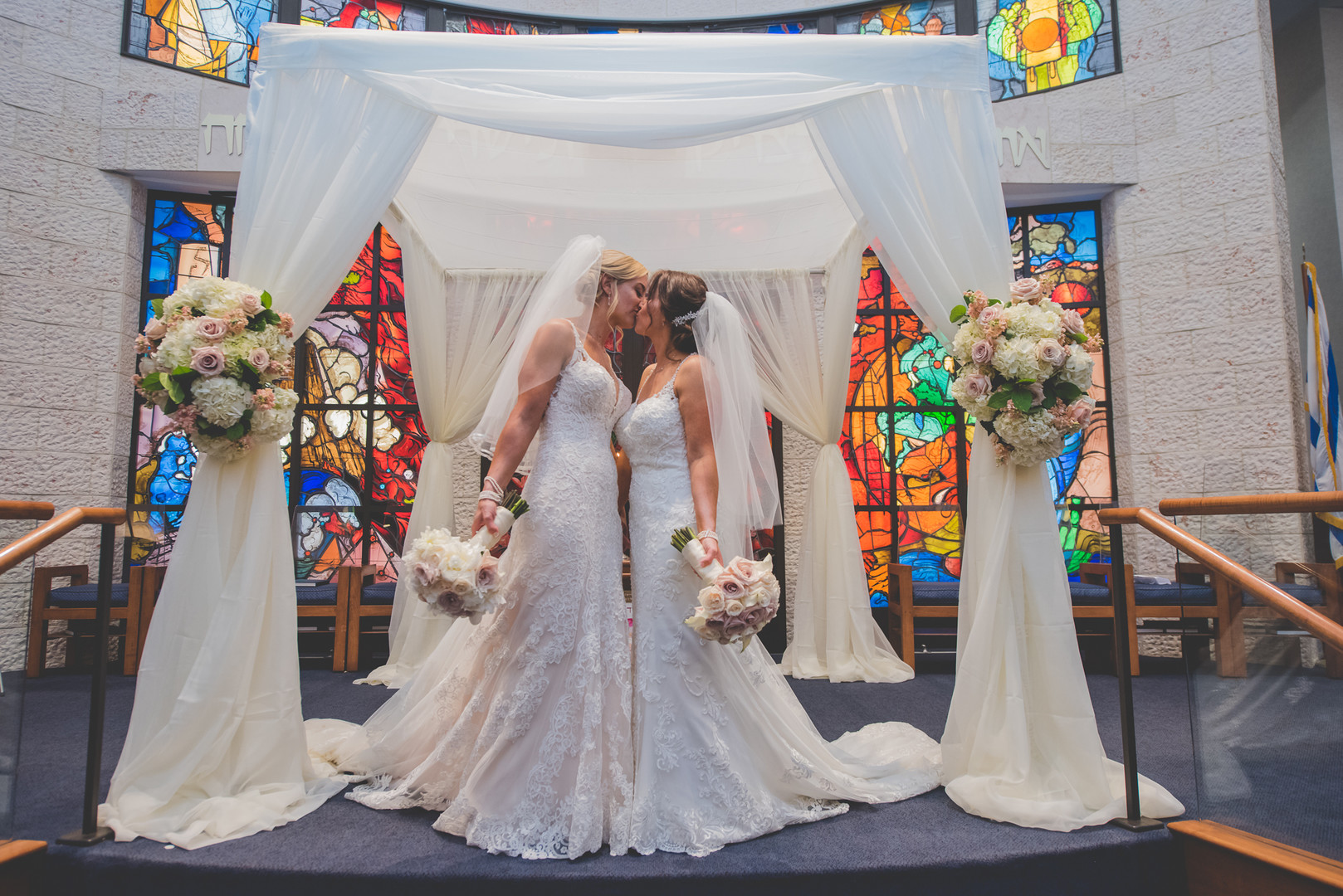 Traditional Jewish wedding during Pride Month two brides up-do long white lace dresses vows kiss