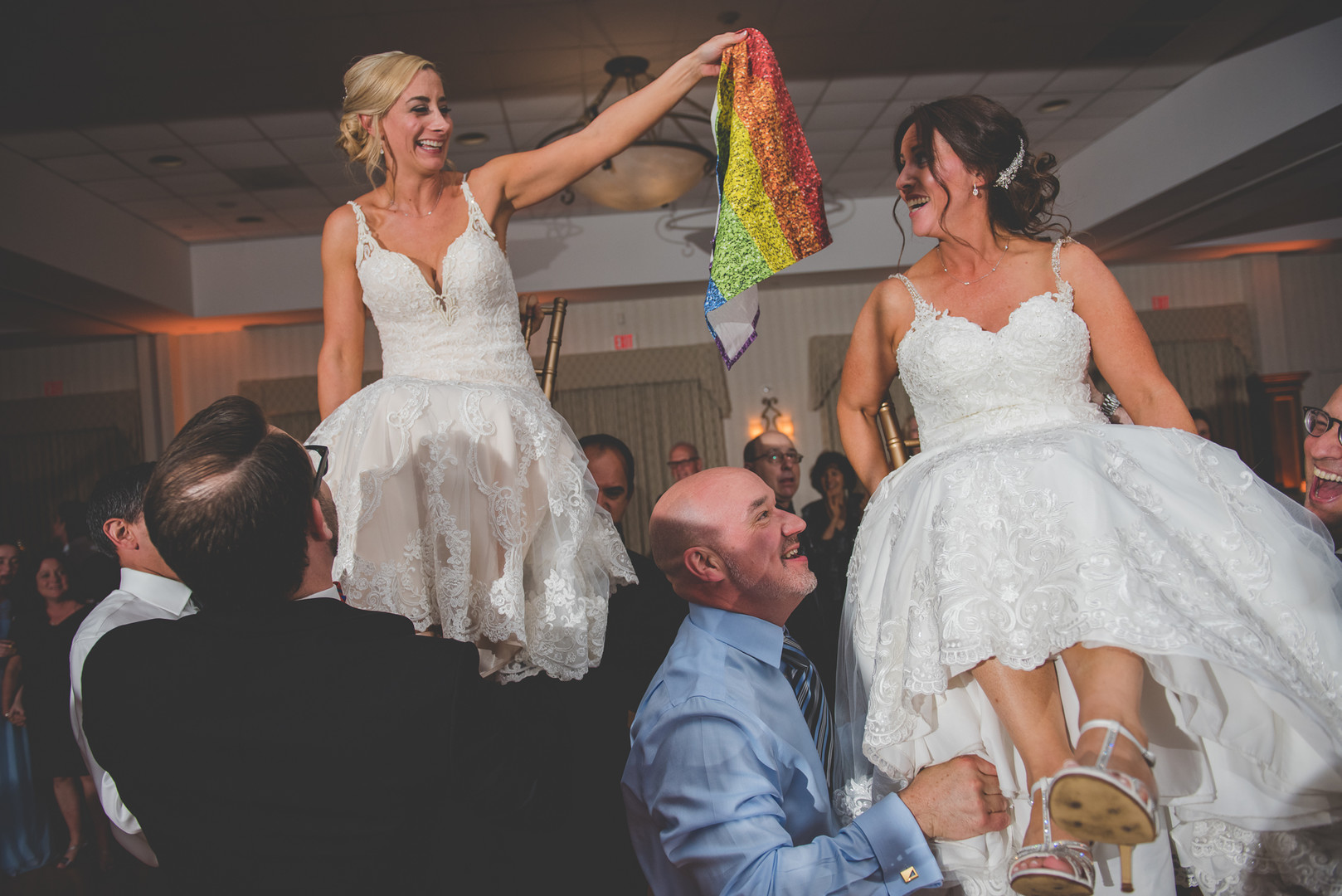 Traditional Jewish wedding during Pride Month two brides up-do long white lace dresses rainbow