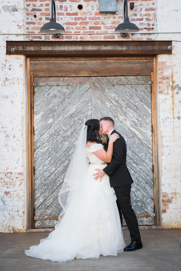 Vintage travel inspired wedding in Monroe, Georgia exposed brick industrial building two brides long white dress veil black tuxedo kiss