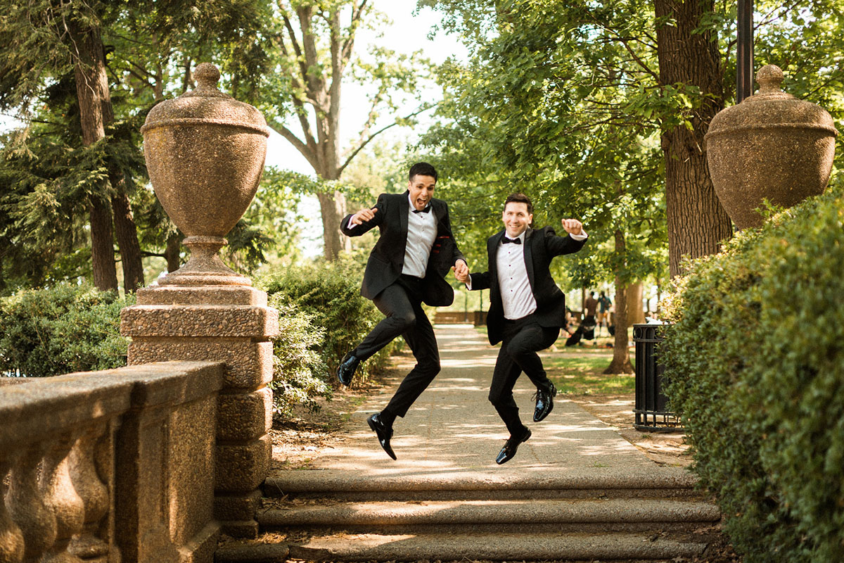 Energetic, colorful wedding in Washington, D.C. two grooms bow ties black tuxedos jumping into the air