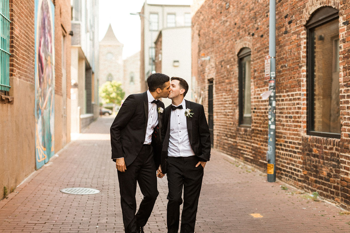 Energetic, colorful wedding in Washington, D.C. two grooms bow ties black tuxedos kiss brick buildings