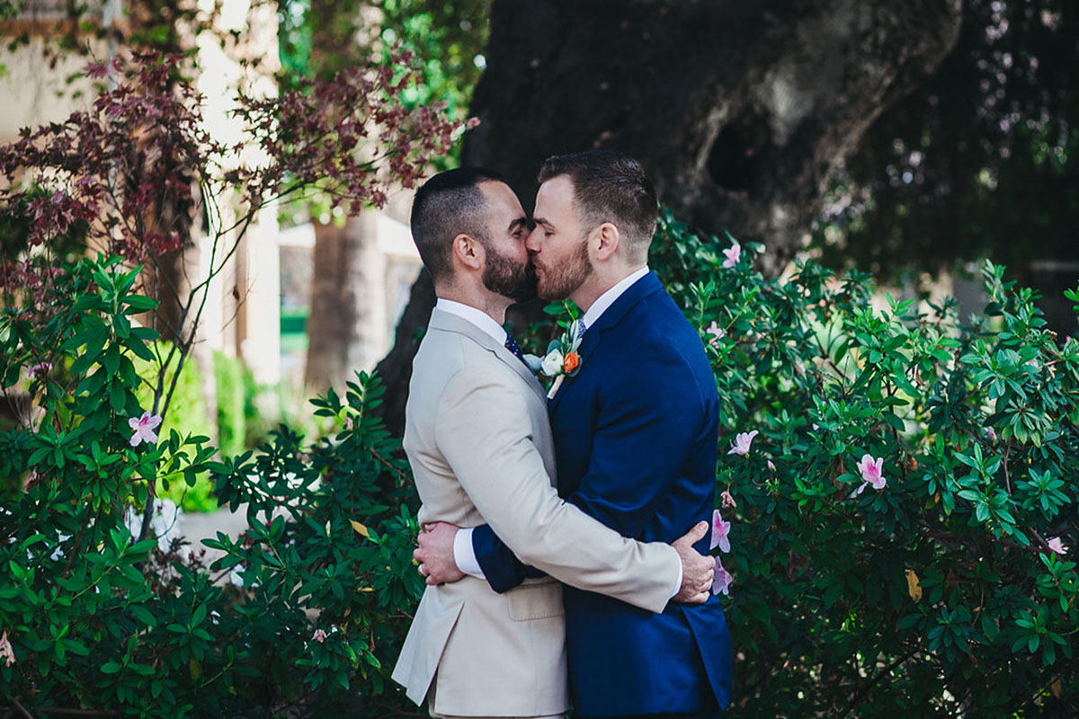 Historic hometown wedding in Pasadena, California two grooms blue tux gray tux boutonnieres kissing outside