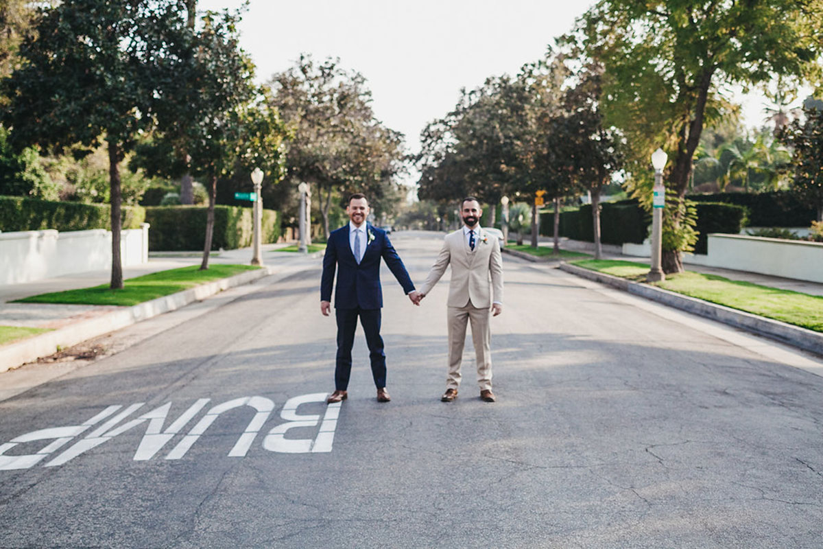 Historic hometown wedding in Pasadena, California two grooms blue tux gray tux boutonnieres outside street holding hands