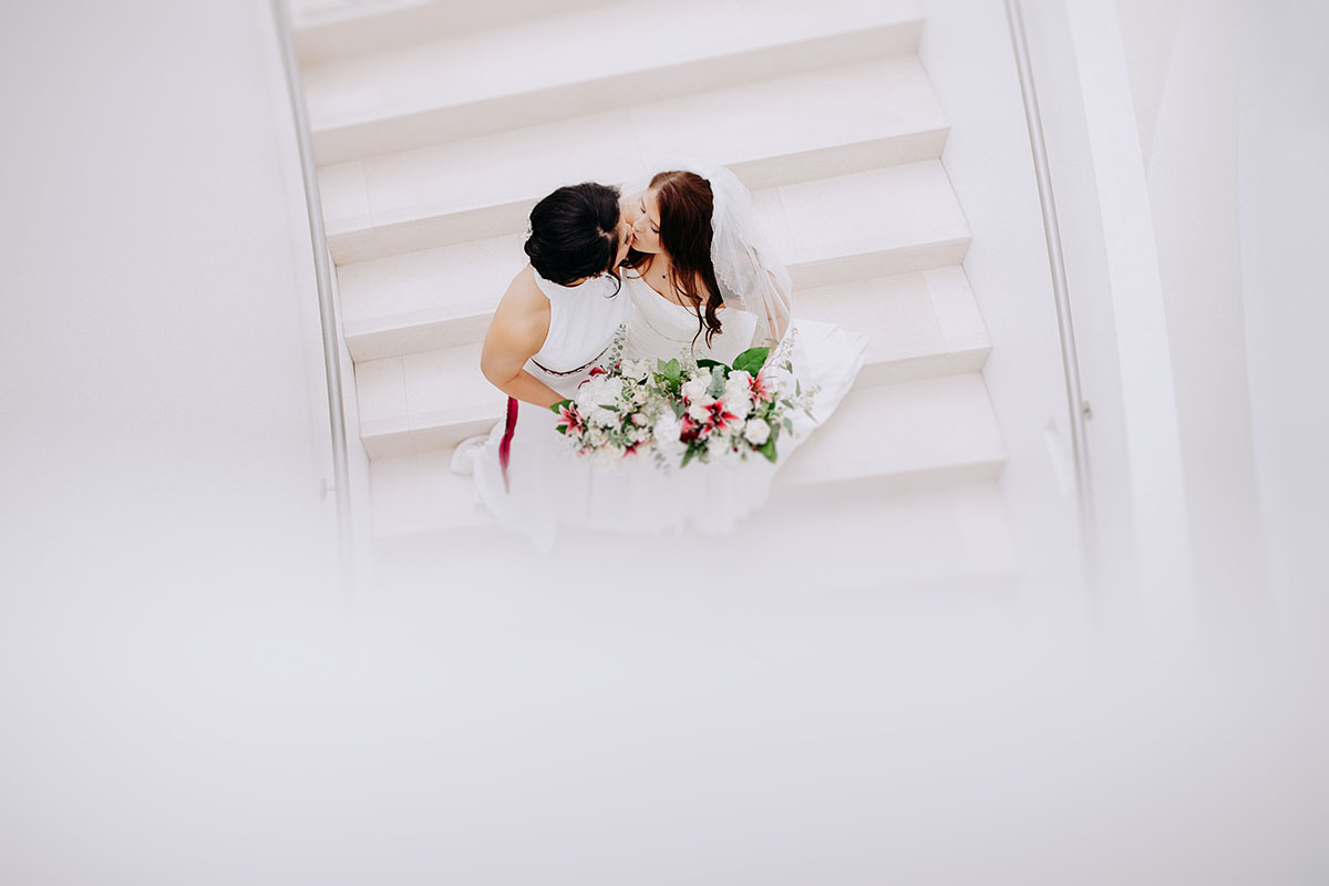 Modern rooftop wedding in Kansas City, Kansas Asian-American lesbian wedding long white dresses staircase kiss
