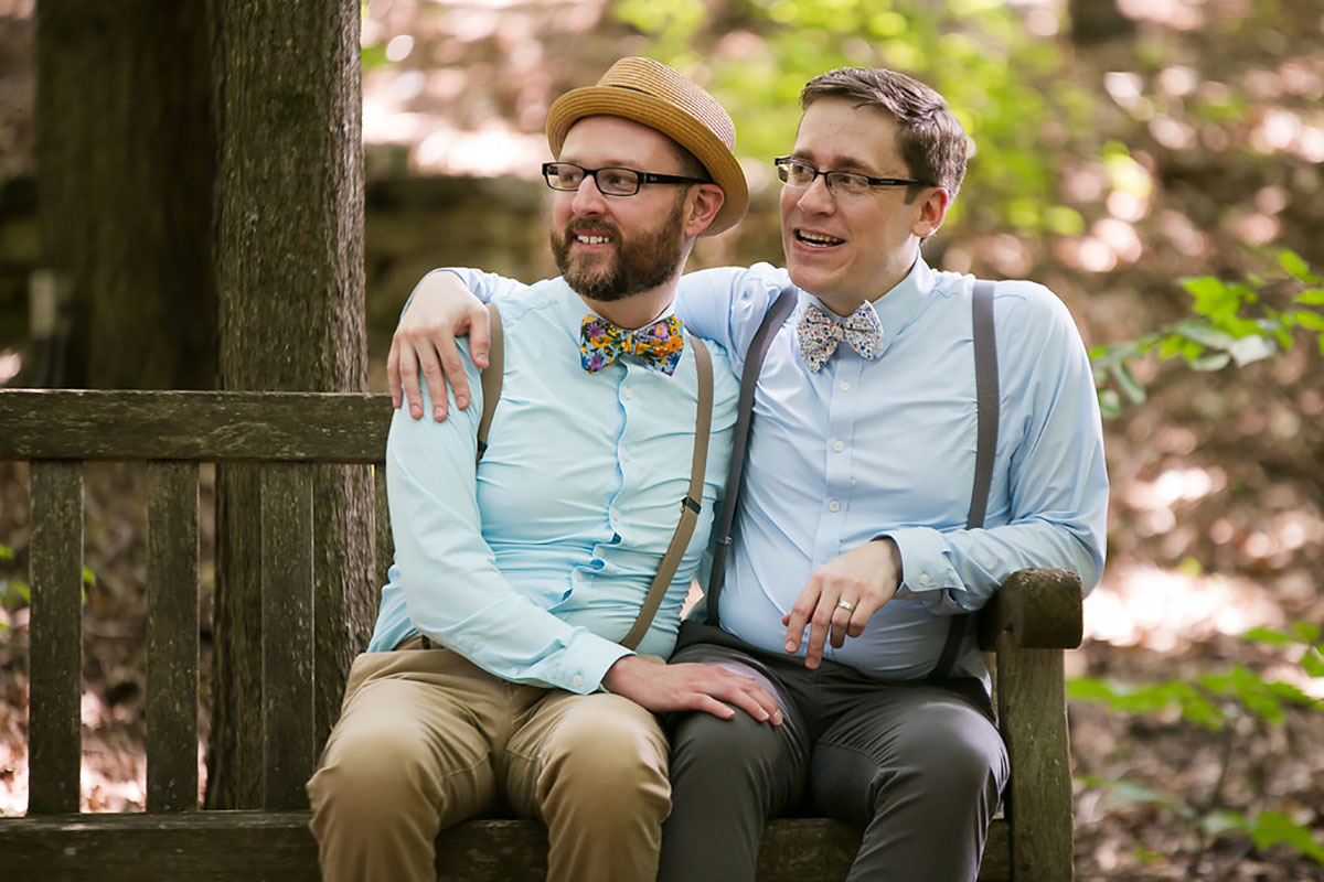 Casual outdoor wedding at the Garden Club of Georgia two grooms suspenders colorful bow ties fun eclectic bench sitting
