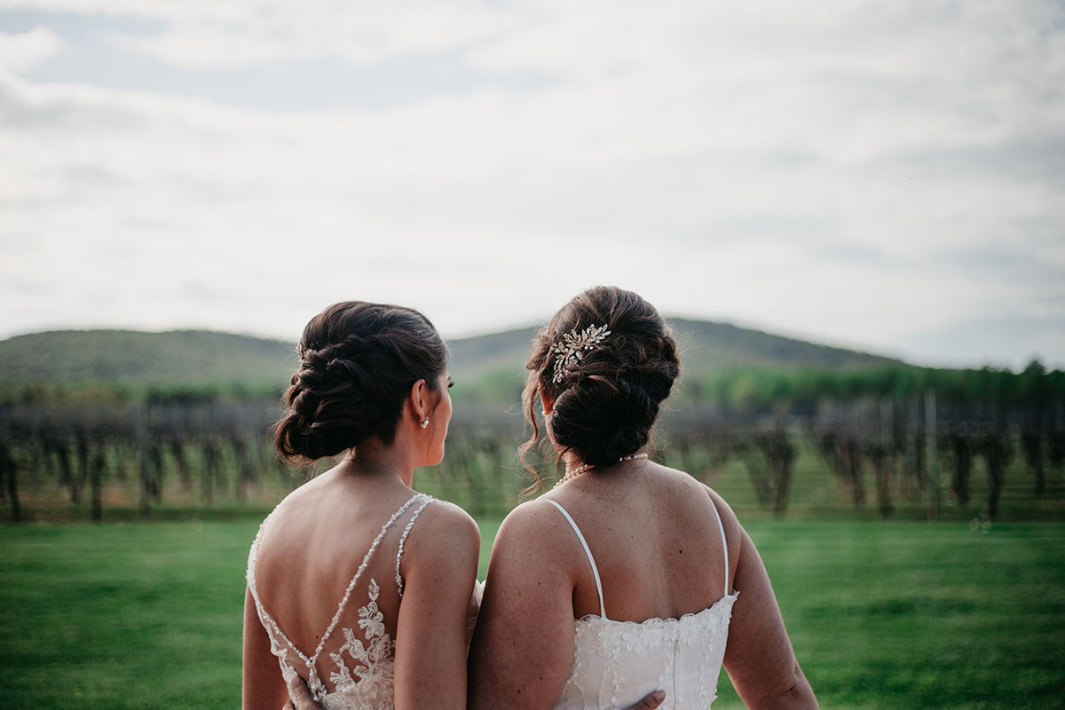 Vintage, romantic vineyard wedding two brides lesbian updos buns white dresses pearls hillside