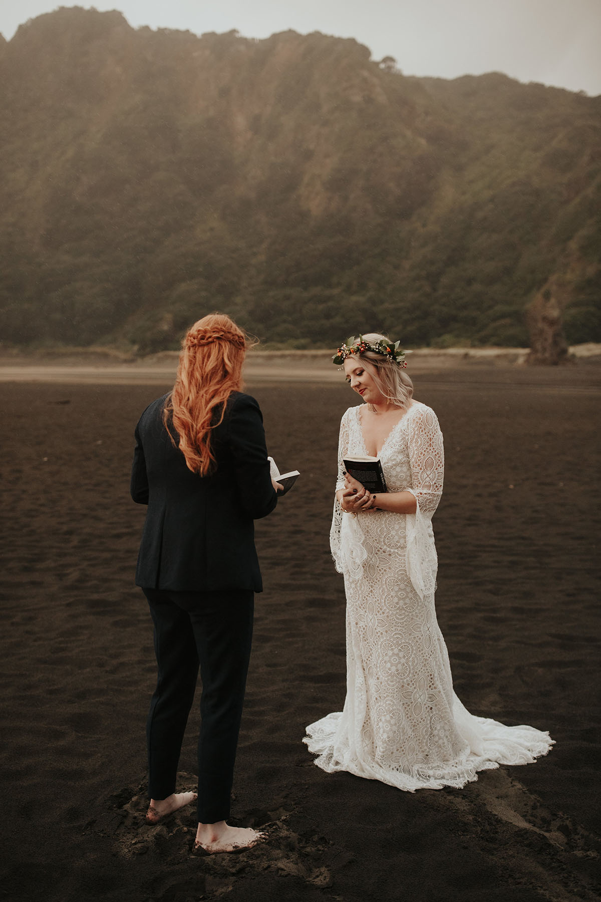 Texas couple elopes to LGBTQ+ friendly New Zealand and their warm, moody beach wedding photos are to die for two brides white lace dress red hair black suit bow tie vows