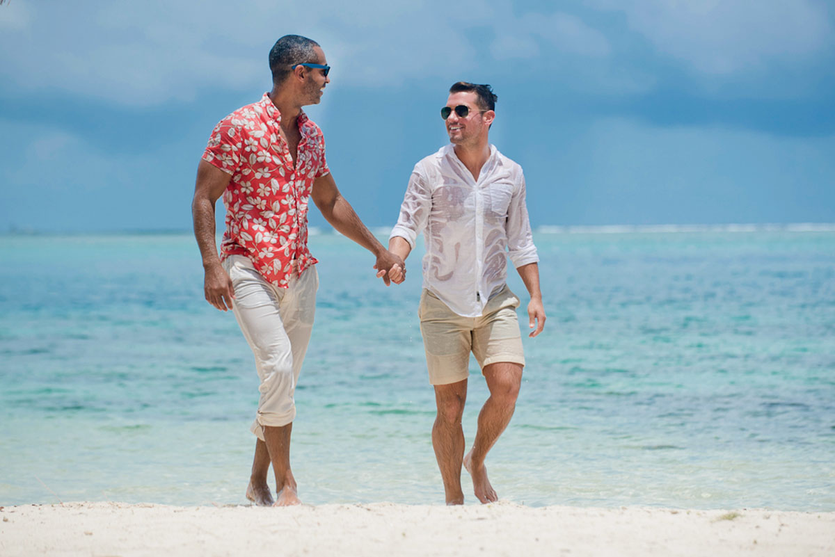 Tropical honeymoon photos on Mo'orea Island two grooms shorts floral pink shirt button down holding hands beach