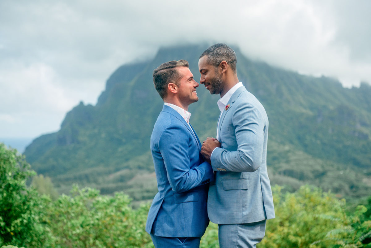 Tropical honeymoon photos on Mo'orea Island two grooms grey suit blue suit mountains outside holding hands