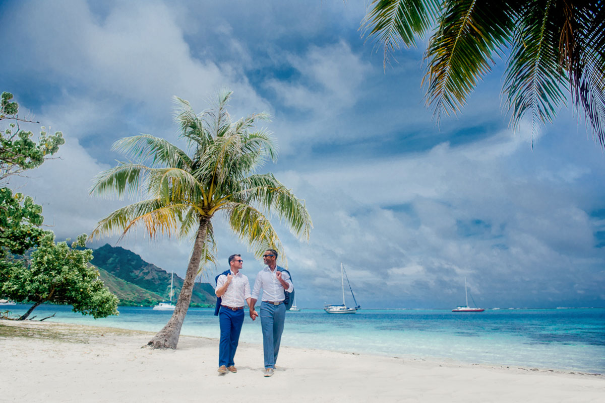 Tropical honeymoon photos on Mo'orea Island two grooms grey suit blue suit mountains outside walking beach
