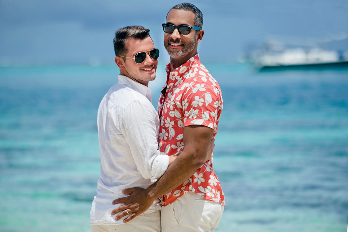 Tropical honeymoon photos on Mo'orea Island two grooms shorts floral pink shirt button down holding each other beach
