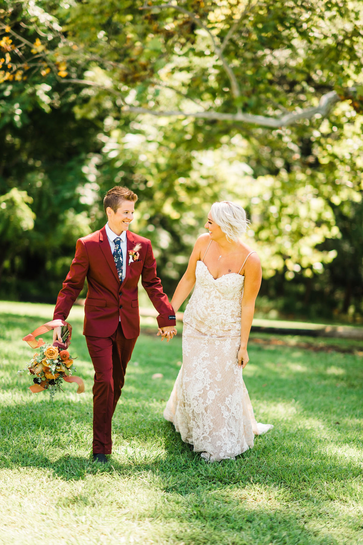Bright bohemian wedding inspiration two brides burgundy red tux white dress colorful flowers long veil holding hands