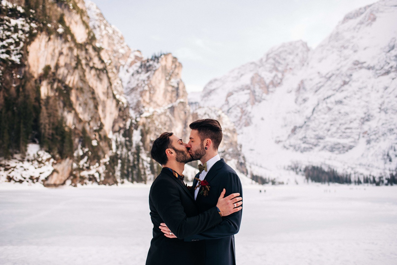 This winter mountain elopement on the Dolomites in Italy is seriously cozy two grooms black tuxedos tux snowy March mountains Lake Braies kiss