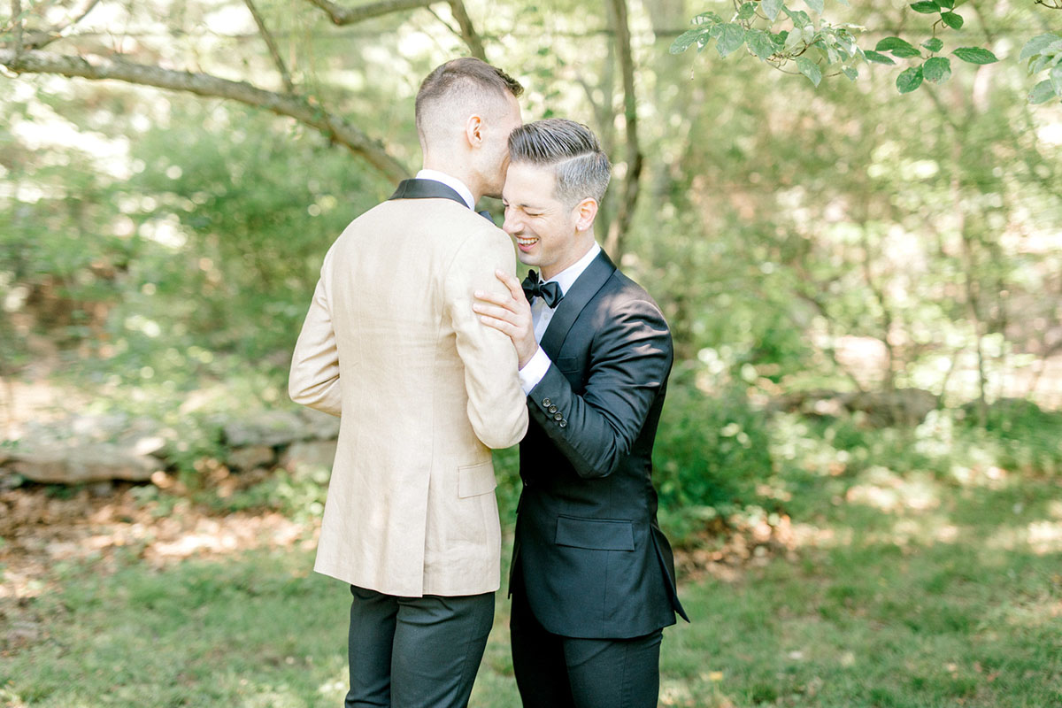 Intimate summer wedding in the woods surrounded by nature two grooms black tux tan tux matching bow ties first look