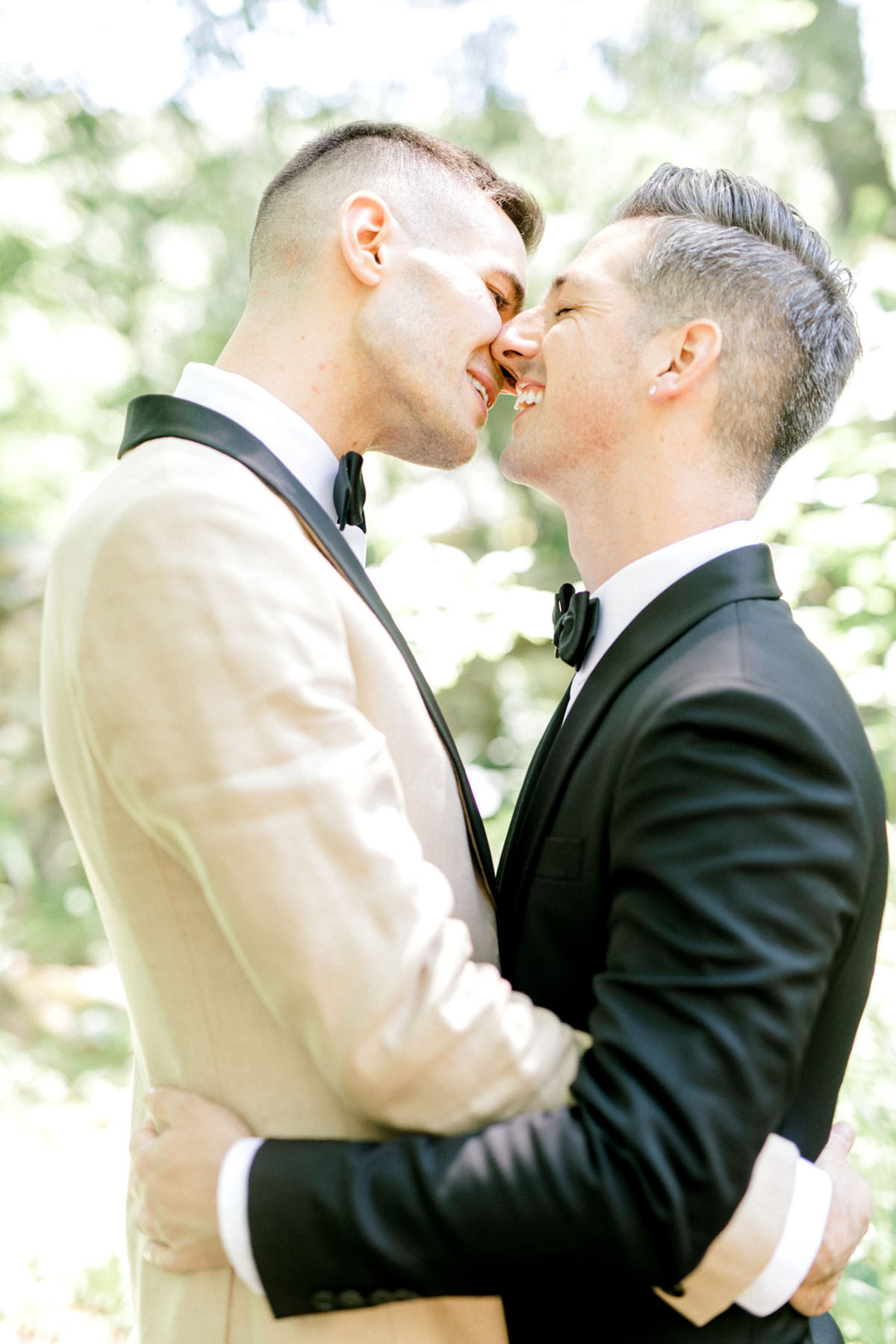 Intimate summer wedding in the woods surrounded by nature two grooms black tux tan tux matching bow ties kiss