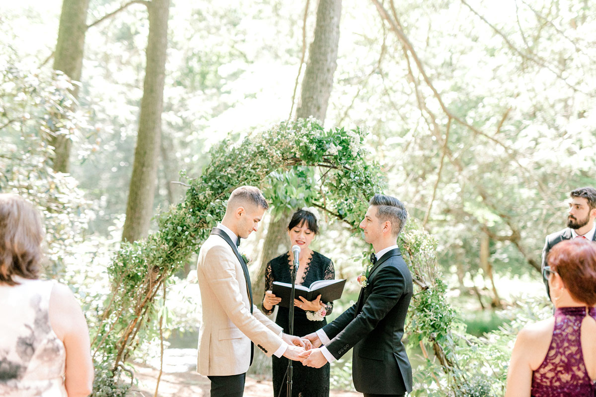 Intimate summer wedding in the woods surrounded by nature two grooms black tux tan tux matching bow ties vows