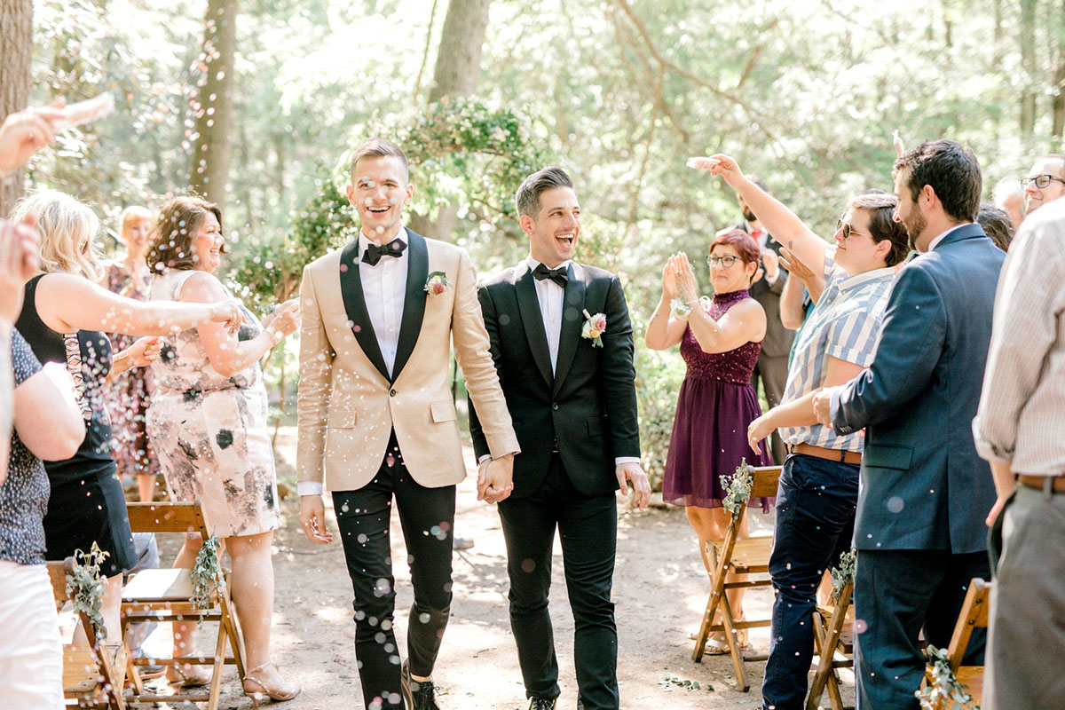 Intimate summer wedding in the woods surrounded by nature two grooms black tux tan tux matching bow ties confetti