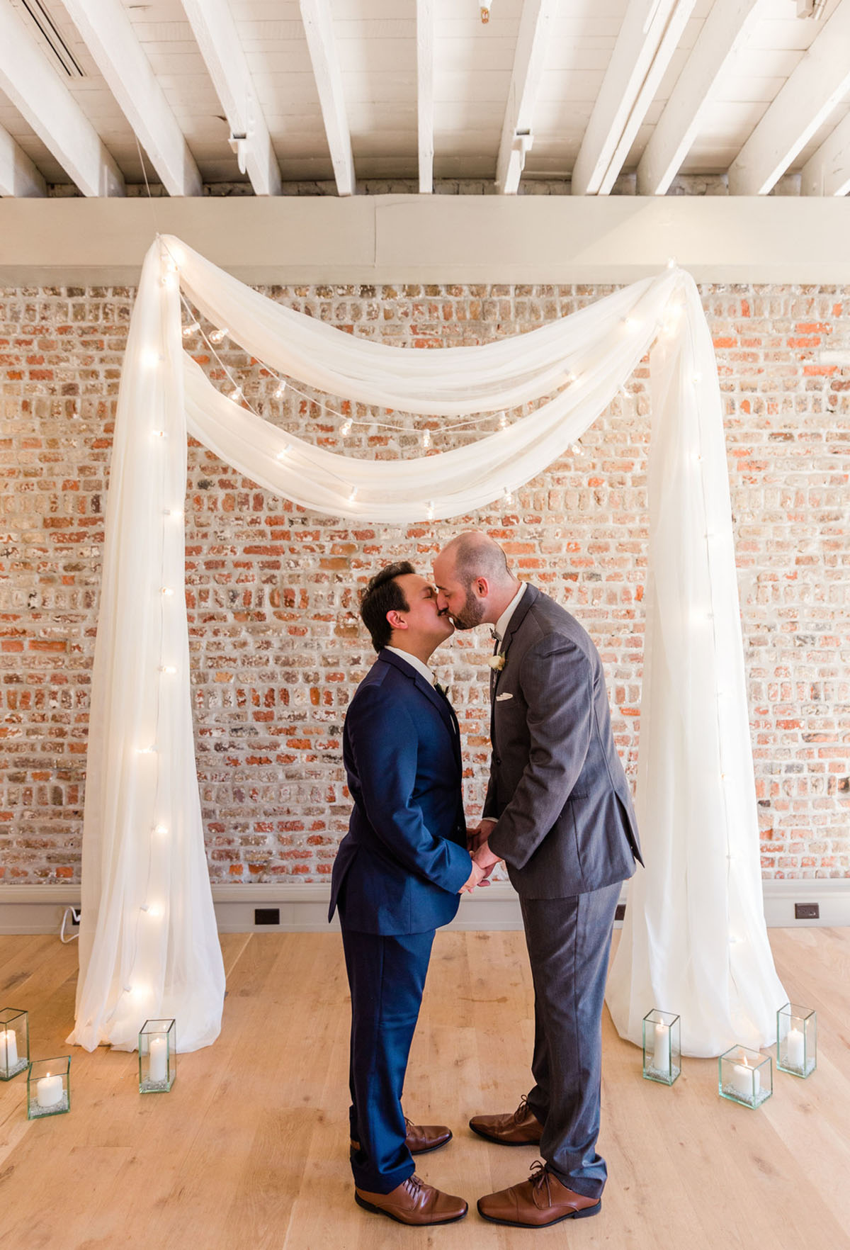 Rustic and romantic wedding inspiration in Charleston, South Carolina two grooms blue tux gray tux oyster shell bow ties fairy lights brick wall kiss