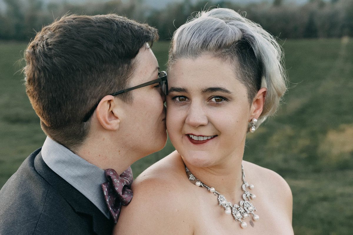 This moody fall ranch wedding in the Blue Ridge Mountains is a dream two brides lesbian wedding colorful boots roller derby skates purple bow tie dark tux white tea length dress crystal necklace rainbow kiss