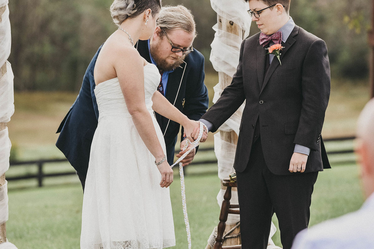 This moody fall ranch wedding in the Blue Ridge Mountains is a dream two brides lesbian wedding colorful boots roller derby skates purple bow tie dark tux white tea length dress crystal necklace rainbow hand tying
