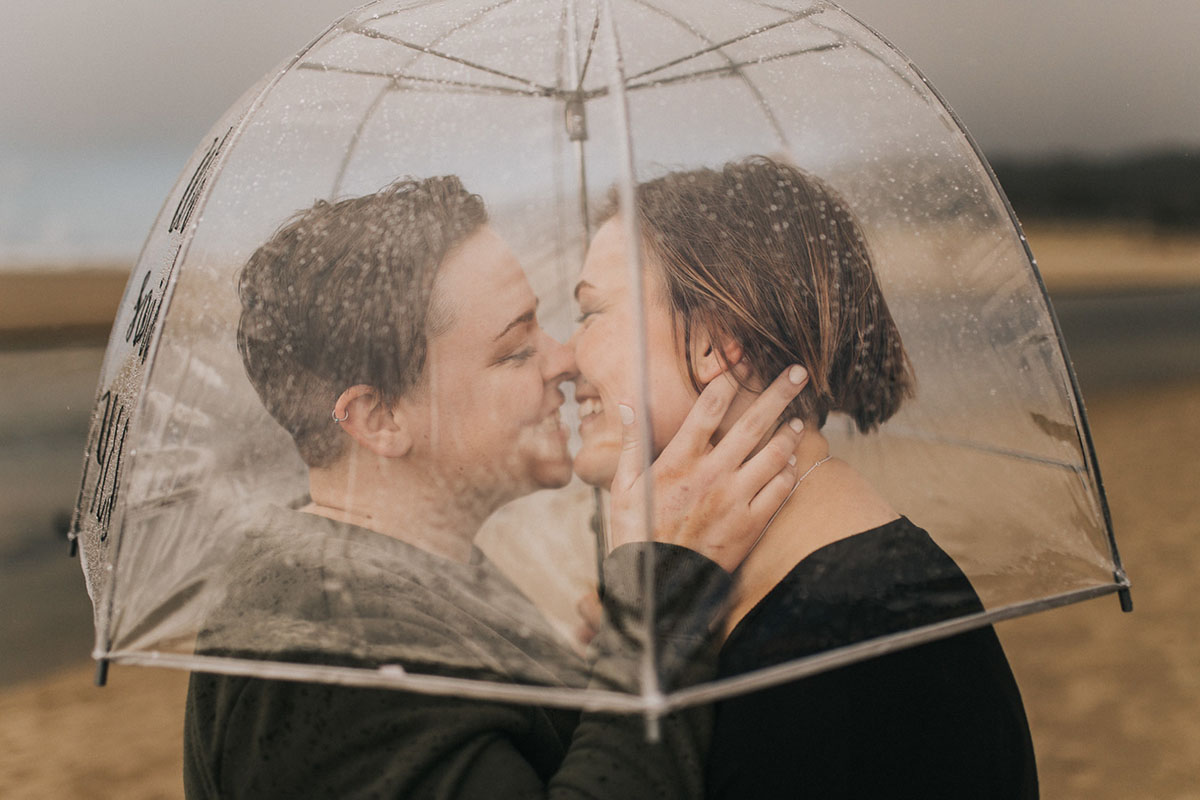 Romantic beach engagement photos on the Oregon Coast two brides Cannon Beach waterfront oceanside rain umbrella