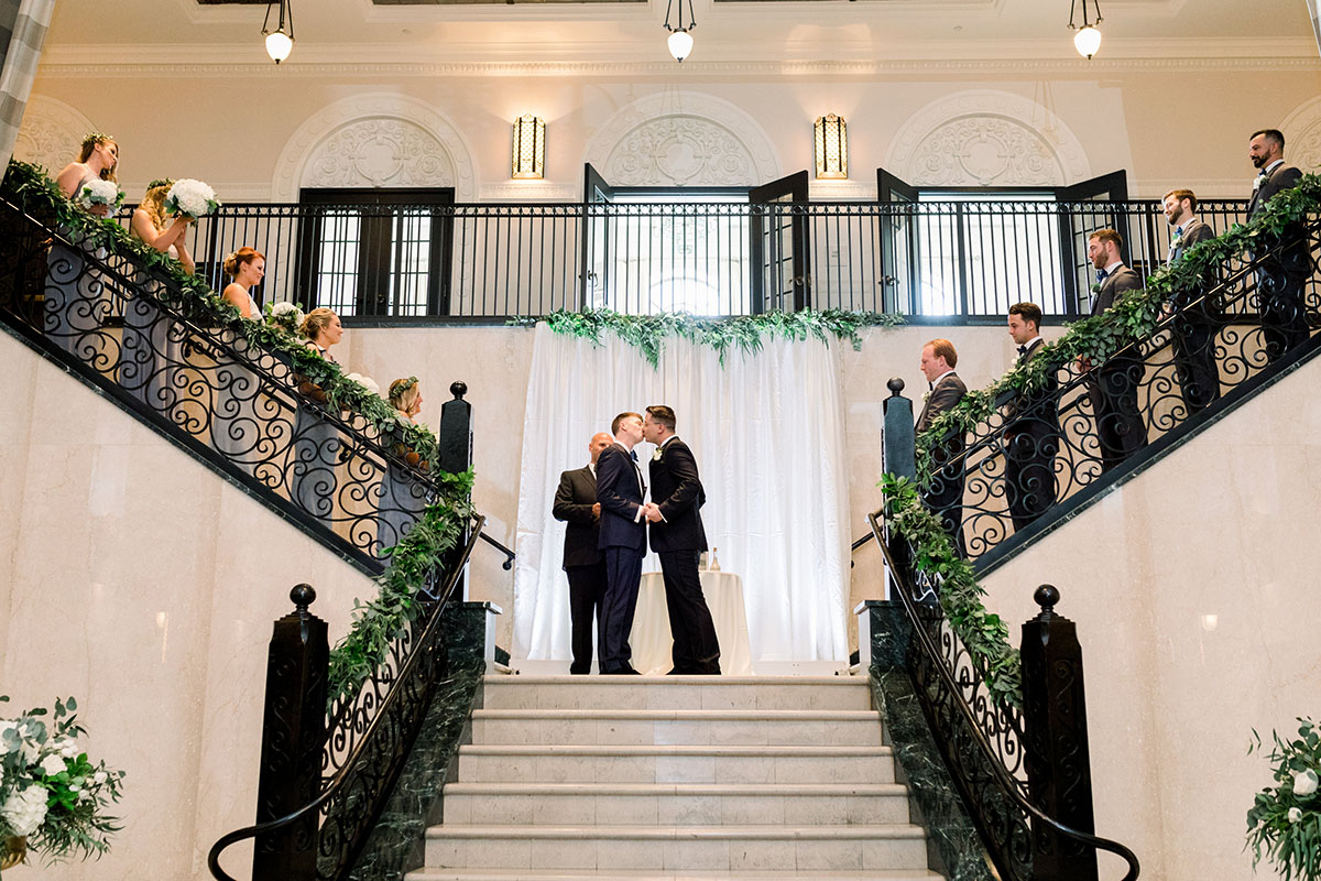Elegant luxe historic hotel wedding in Tulsa, Oklahoma two grooms tuxedos bow ties luxurious gay wedding kiss