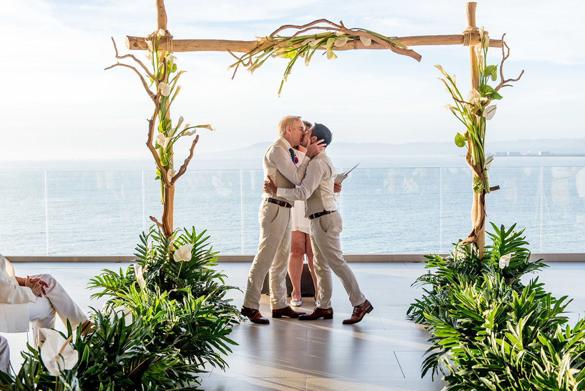 Tropical destination white beach wedding in Puerto Vallarta, Mexico two grooms linen tailored suits tradition whimsical kiss