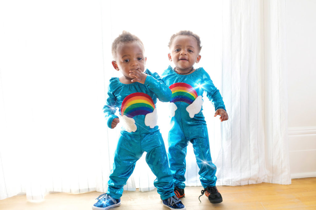 Don't make these 5 mistakes when choosing a sperm bank. photo description: twins standing in front of a window in matching blue jumper suits with rainbows and clouds.