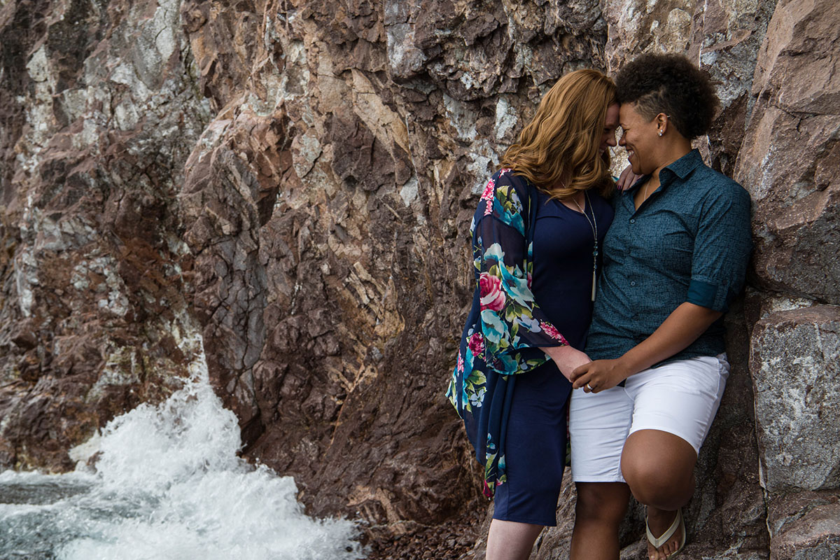 Fun waterfront engagement photos on the coast of Lake Superior rocks waves dark blue outfits smiling