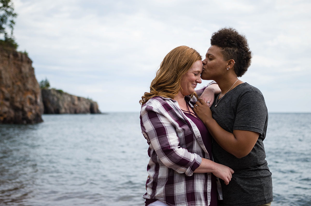 Fun waterfront engagement photos on the coast of Lake Superior beach forehead kiss