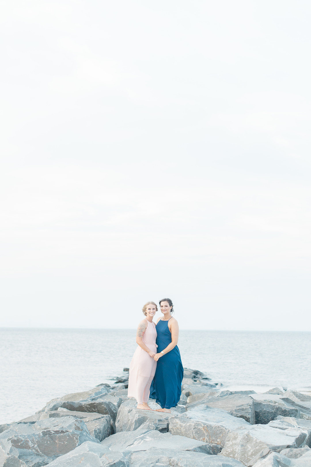 Beach engagement photos at Bayshore Waterfront Park two brides same-sex engagement pink dress blue dress rocks