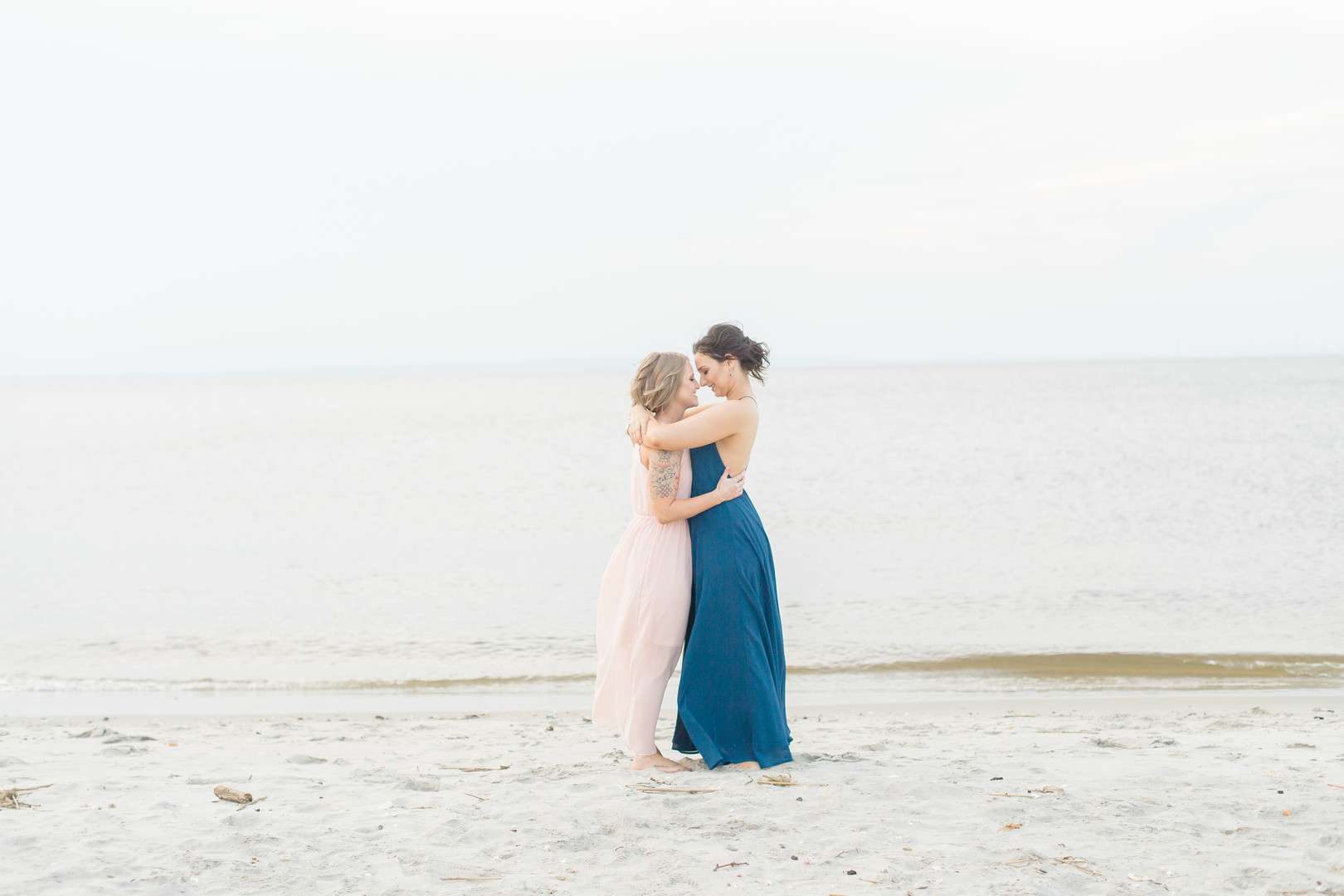 Beach engagement photos at Bayshore Waterfront Park two brides same-sex engagement pink dress blue dress embrace