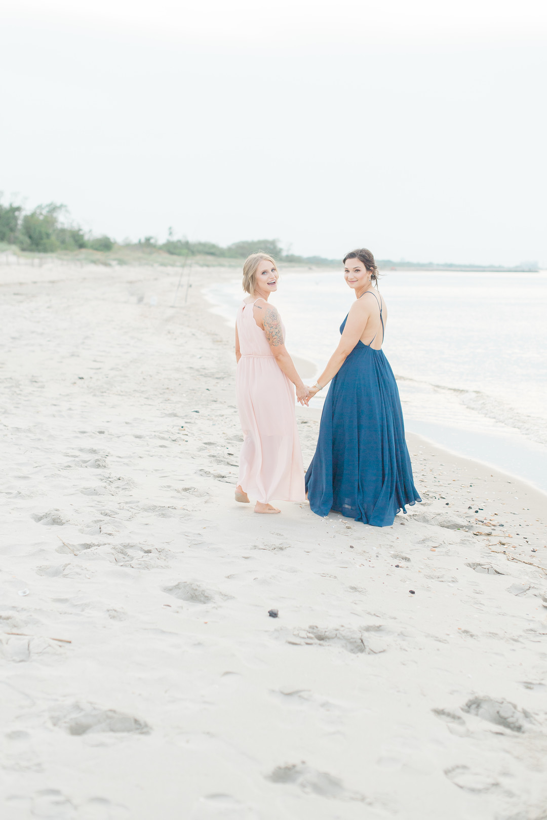 Beach engagement photos at Bayshore Waterfront Park two brides same-sex engagement pink dress blue dress holding hands
