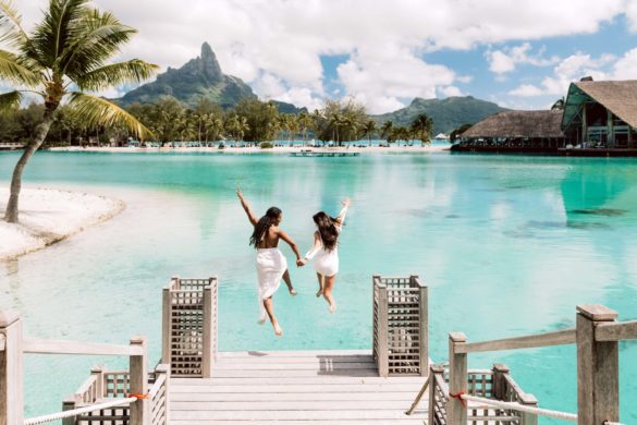 Beach honeymoon photos in Bora Bora two brides white dresses clear blue oceans palm trees jump in