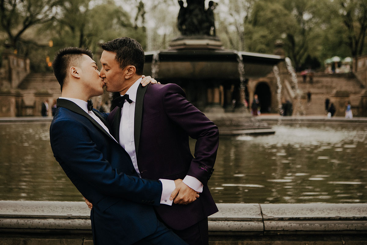 Elegant, fun engagement photos at Central Park with rainbow bubbles two grooms purple tux blue tux bow ties fountain
