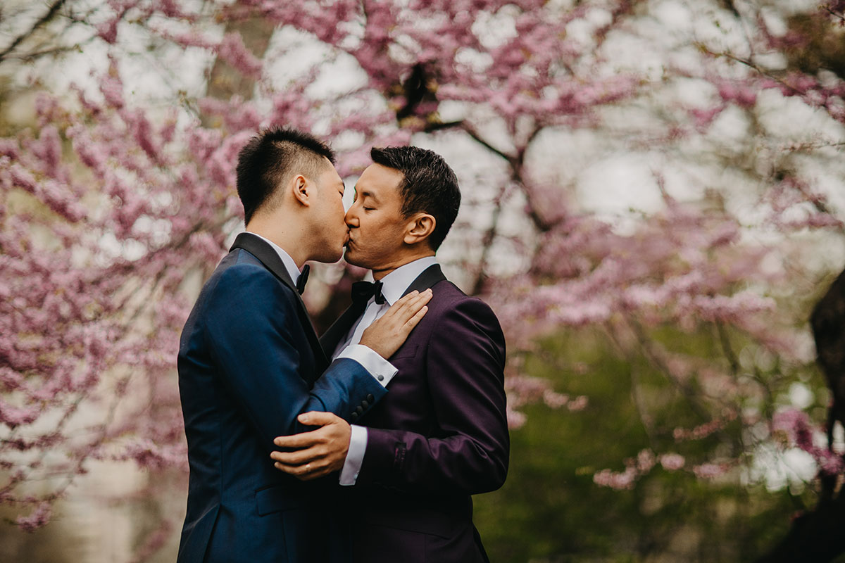 Elegant, fun engagement photos at Central Park with rainbow bubbles two grooms purple tux blue tux bow ties kiss pink tree
