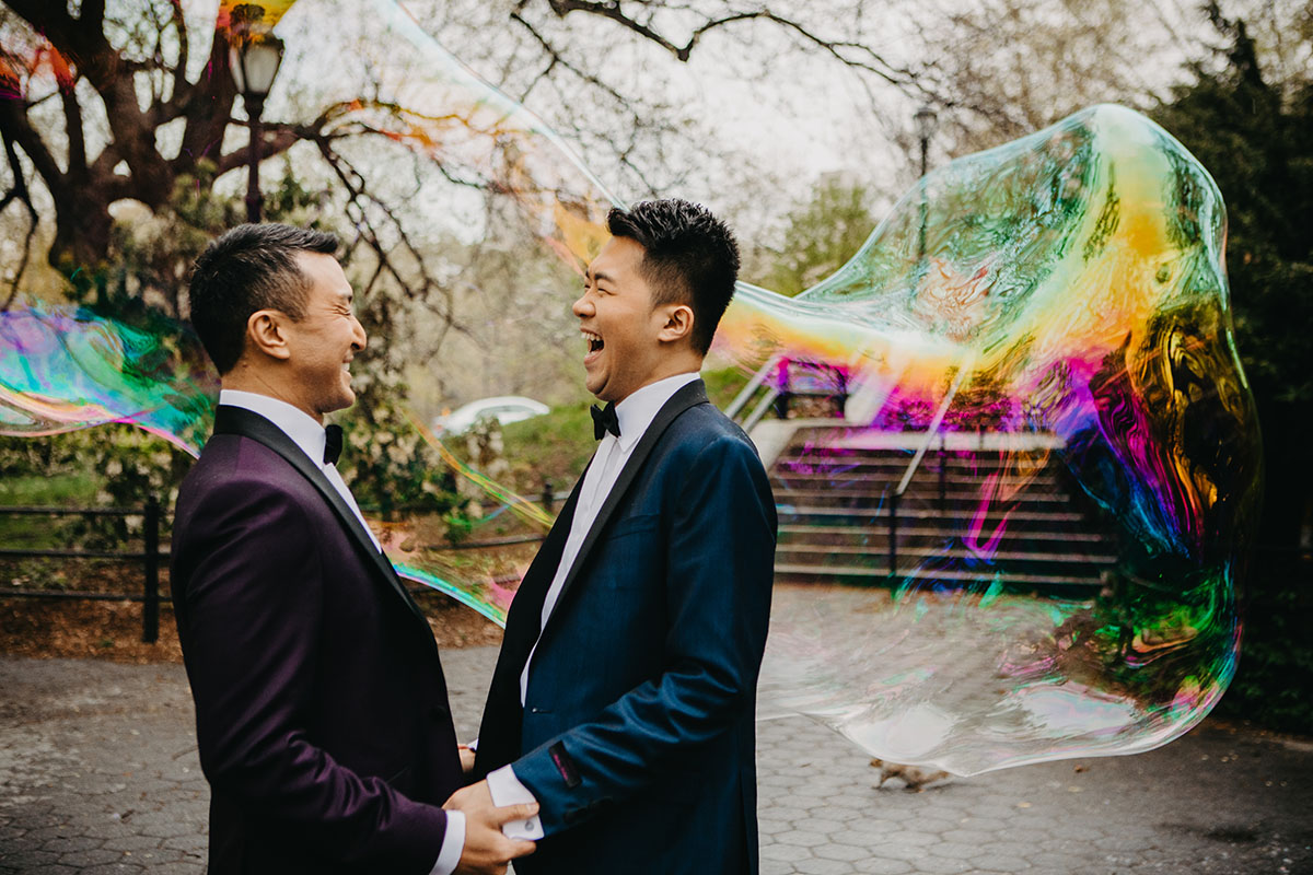 Elegant, fun engagement photos at Central Park with rainbow bubbles two grooms purple tux blue tux bow ties laugh