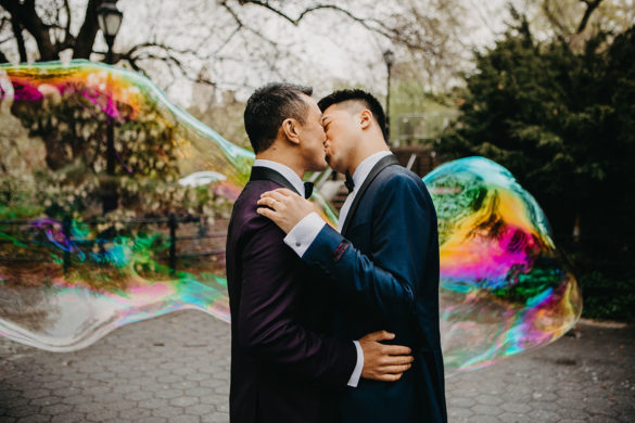 Elegant, fun engagement photos at Central Park with rainbow bubbles two grooms purple tux blue tux bow ties kiss