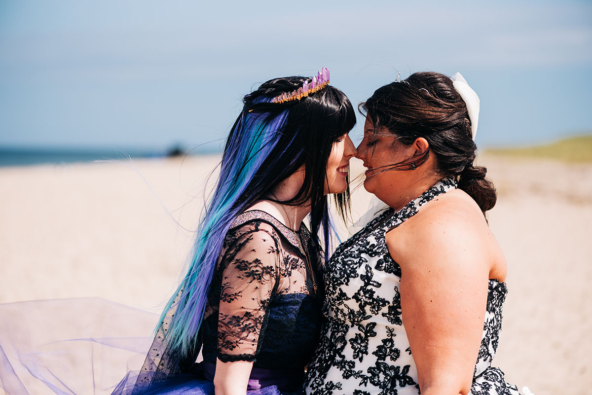 High school sweethearts marry after 10 years in colorful beach ceremony LGBTQ+ weddings beach summer wedding Provincetown two brides lesbian wedding rainbow nontraditional whimsical creative book literary library