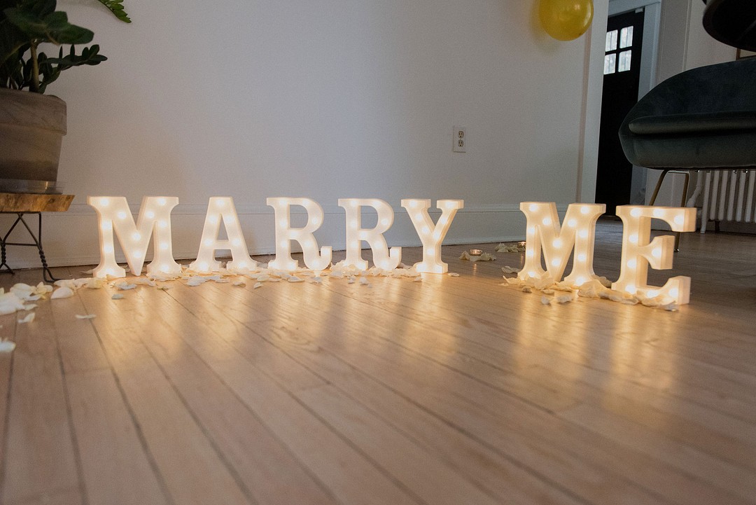 Intimate at-home proposal surrounded by chosen family LGBTQ+ weddings two brides Ruth Bader Ginsberg Washington DC Marry Me engaged engagement candles wine