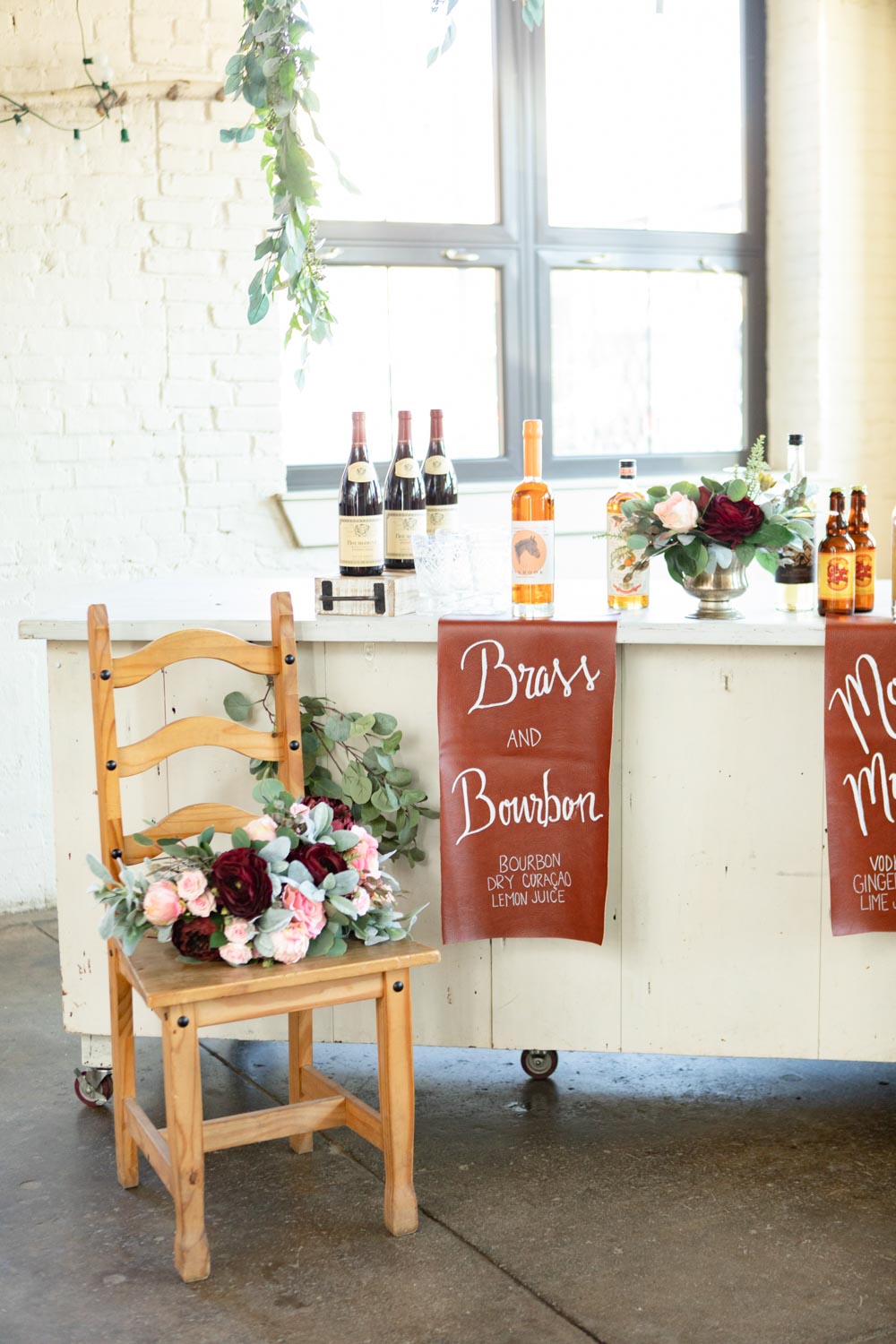 An all-female vendor team created this gorgeous burgundy and gold LGBTQ+ wedding inspiration at The White Room in Worcester, Massachusetts. The venue is situated in a historic mill building. The models are a real-life couple who are getting married this October. We love the burgundy contrasted with blush, rusty orange and the leather and gold touches.